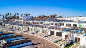A modern hotel with multiple levels, outdoor seating areas, and a clear view of the surrounding palm trees. - Bright dog-friendly home with heated pool, hot tub, streaming, & ocean views (Rosarito)
