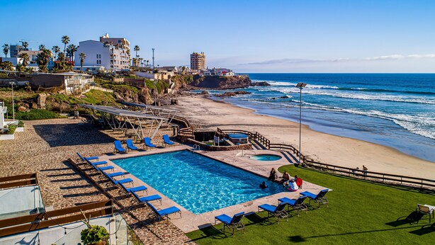 A pool area with blue lounge chairs, a small pool, and a view of the ocean. - Dog-friendly villa with heated pool, hot tub, streaming, partial ocean views (Rosarito)