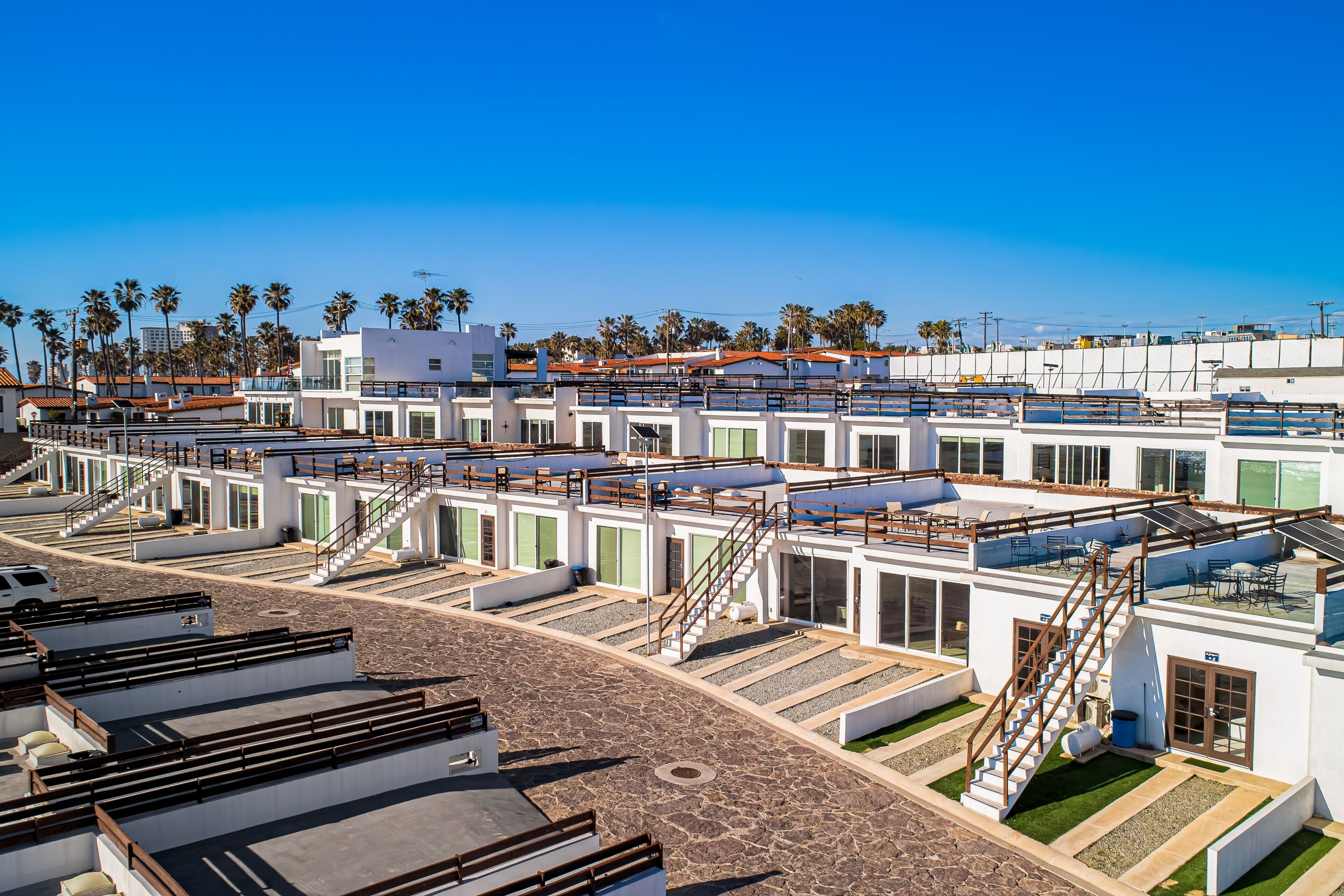 Un hôtel à étages, doté de terrasses extérieures et offrant une vue dégagée sur les palmiers et les bâtiments environnants.