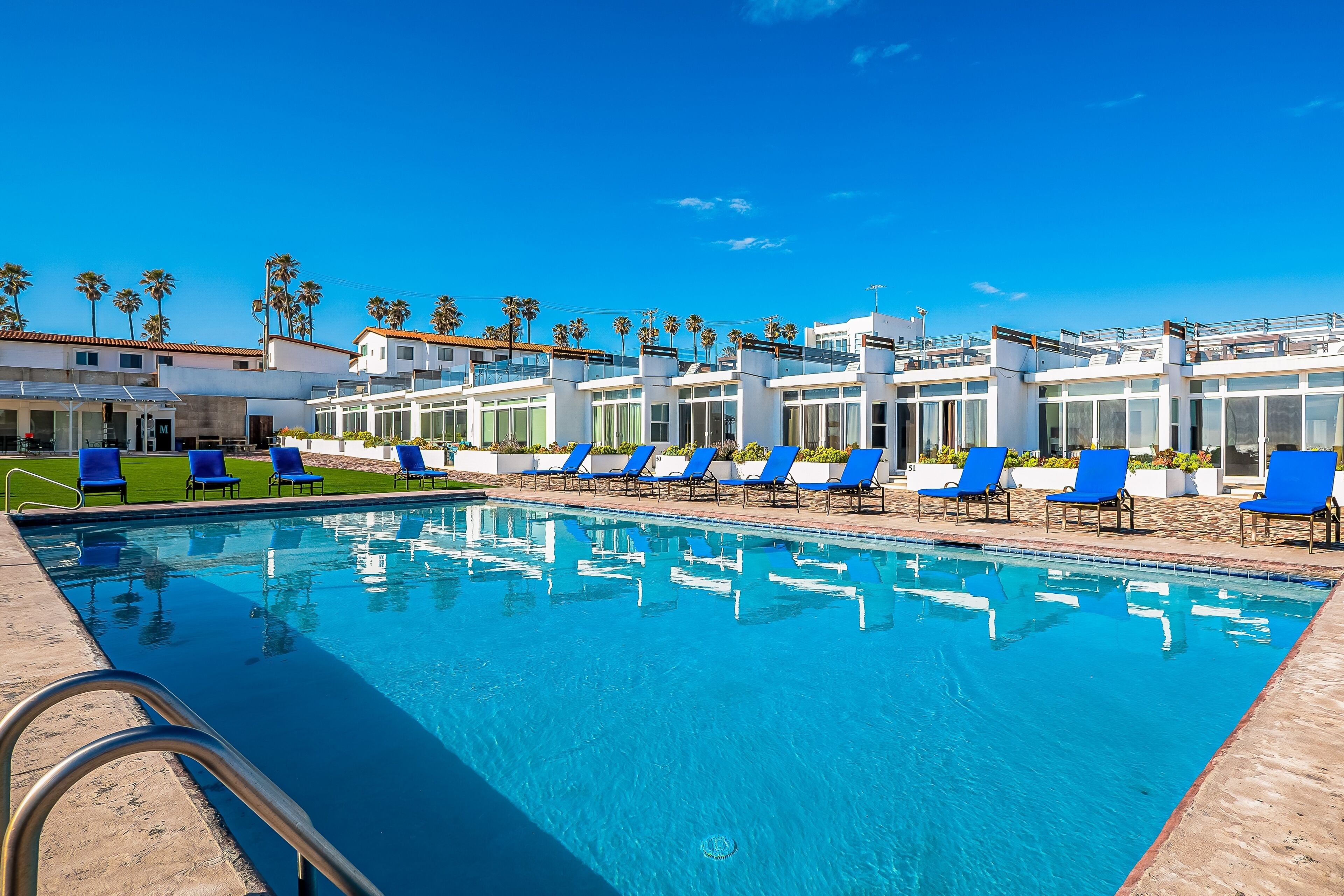 A swimming pool with blue lounge chairs and palm trees in the background.