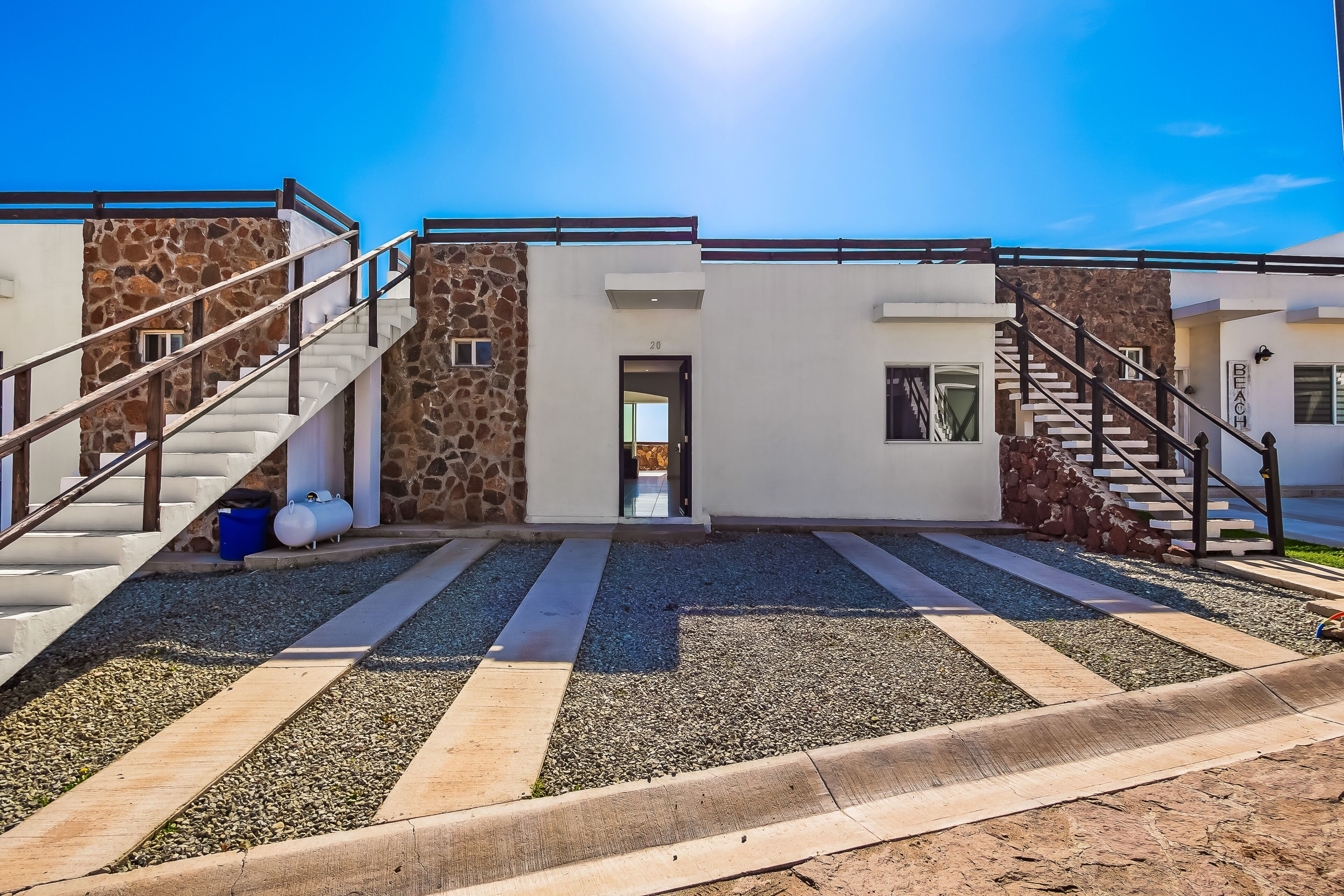A modern building with two staircases, a stone wall, and a gravel pathway.
