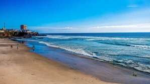 Ein Strand mit einem Gebäude links und brechenden Wellen.