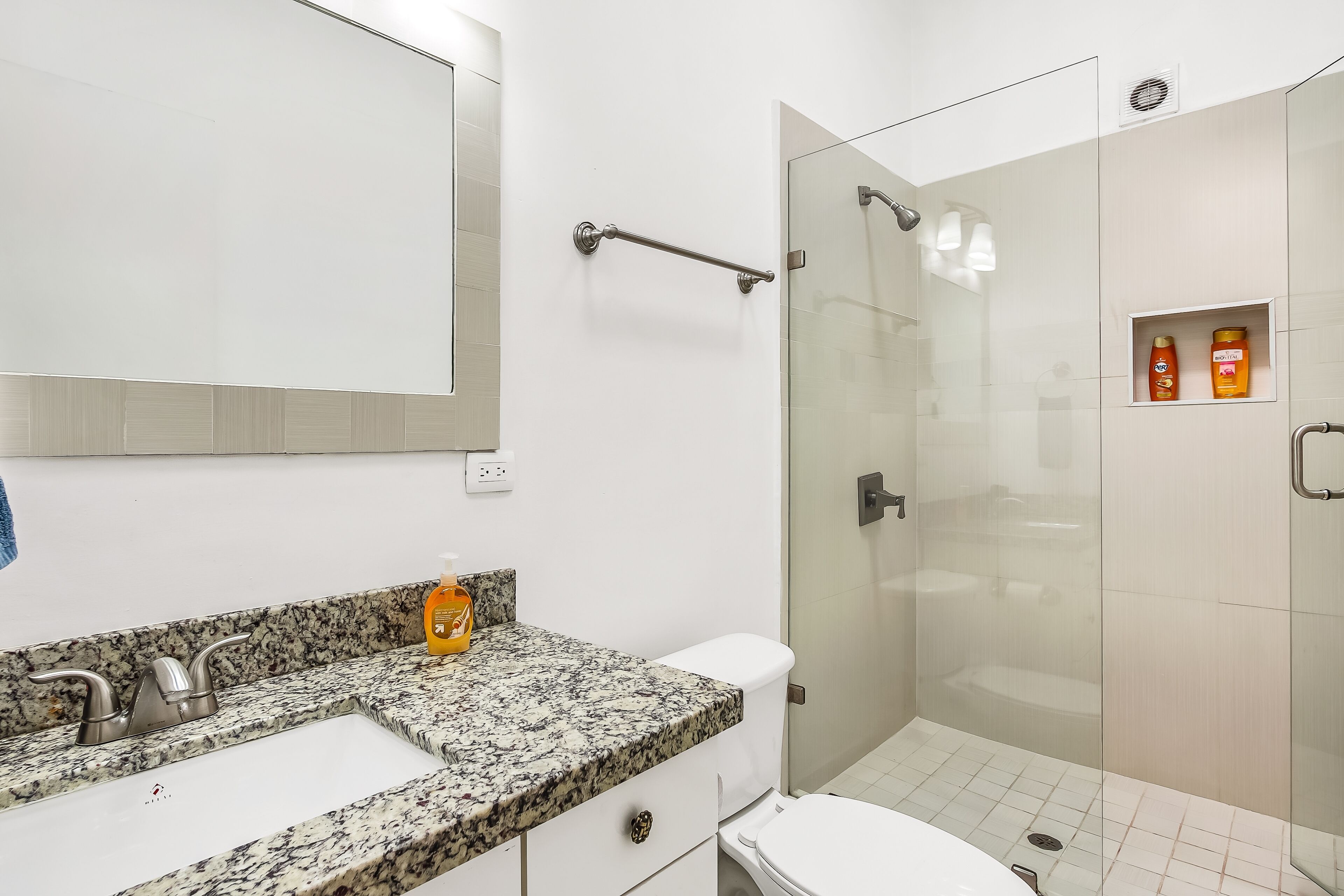 A modern bathroom with a granite countertop, a white sink, a toilet, and a glass-enclosed shower area.