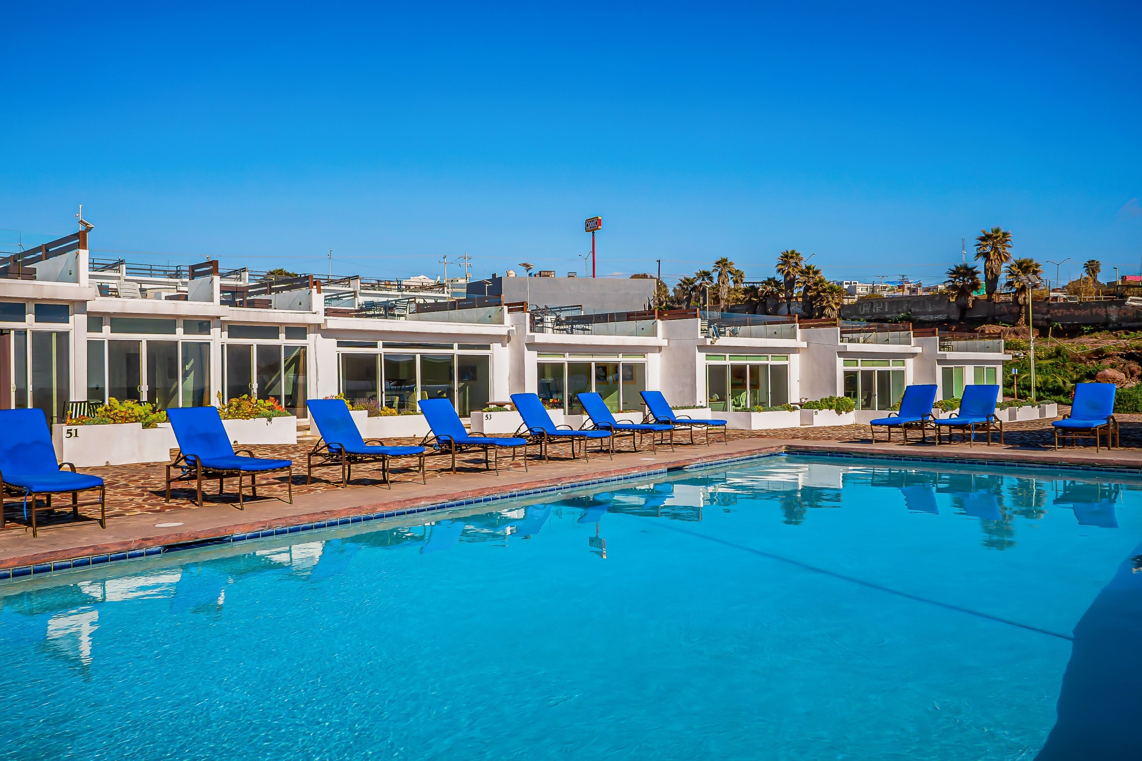 Ein Swimmingpool mit blauen Liegestühlen und ein Gebäude mit großen Fenstern im Hintergrund.