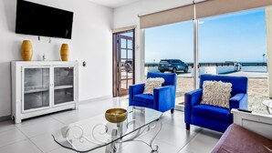 A modern living room with a glass coffee table, two blue armchairs, a white cabinet, and a large TV. - Dog-friendly villa with heated outdoor pool, hot tub, streaming, private patio (Rosarito)