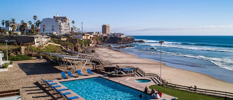 A beachfront hotel with a swimming pool, sun loungers, and a view of the ocean.