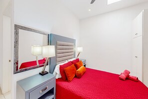 Ein modernes Schlafzimmer mit roter Bettdecke, einem großen Spiegel, Nachttischlampen und einer grauen Kommode.