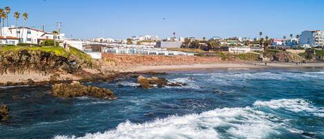 A coastal view with rocky shoreline, waves, and buildings in the background.