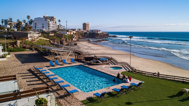 A beachfront hotel with a swimming pool, sun loungers, and a view of the ocean.