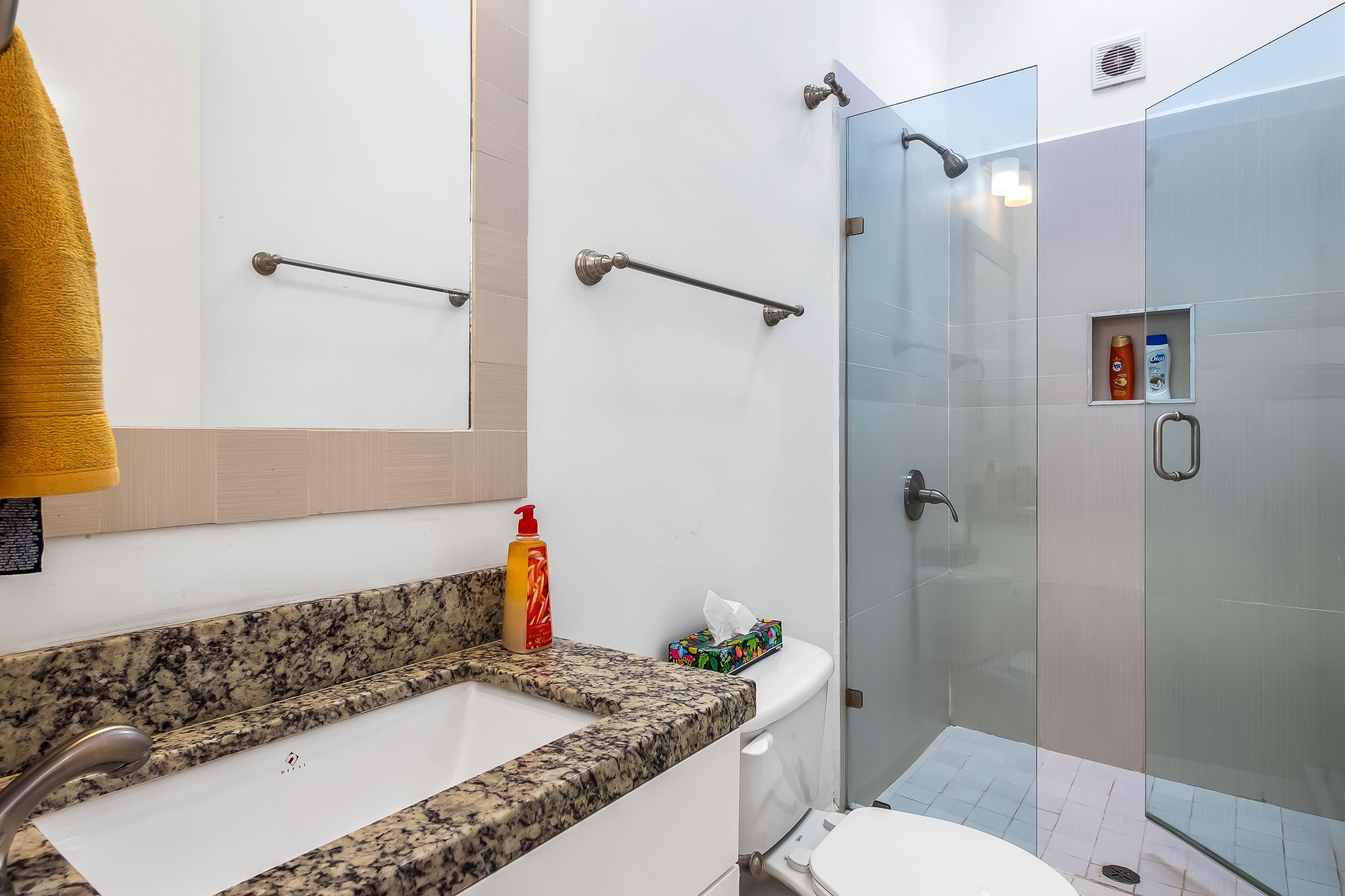 A modern bathroom with a granite countertop, a white toilet, and a glass-enclosed shower.