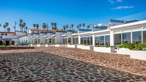 A paved outdoor area with modern buildings, palm trees, and outdoor seating.