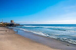 Una playa con un edificio a la izquierda, cielos despejados y olas.
