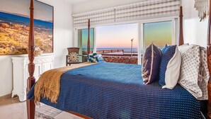 A bedroom with a large bed, a view of the sunset, and a painting on the wall. - Dog-friendly ocean-view villa with patio, outdoor pool, streaming, partial AC (Rosarito)