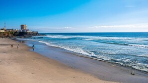 A beach with a clear sky, waves, and a few people walking. - Dog-friendly ocean-view villa with patio, outdoor pool, streaming, partial AC (Rosarito)