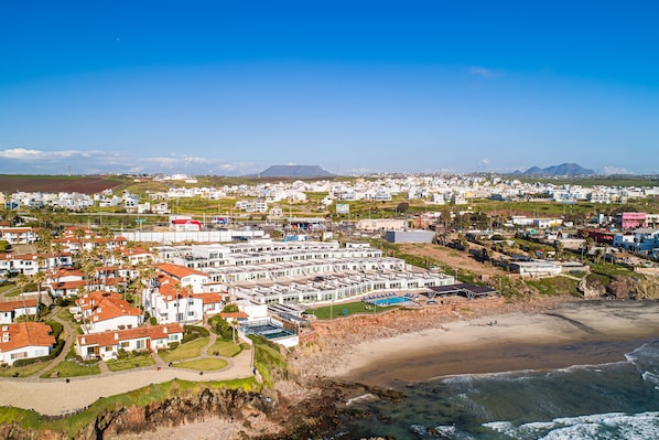 A coastal residential area with white buildings, a beach, and a clear blue sky.