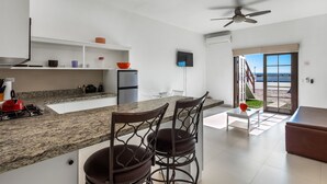 Eine moderne Küche mit Granit-Arbeitsplatten, einem Gasherd und einem Deckenventilator. Ein Essbereich mit Tisch und Stühlen lädt zum Verweilen ein, und durch eine Glastür eröffnet sich der Blick nach draußen.