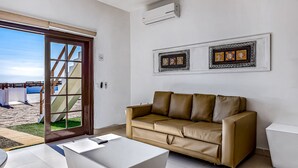 Una sala de estar moderna con un sofá de cuero color beige, una mesa de centro blanca y un gran ventanal corredizo que da a un espacio exterior con vistas a la playa.