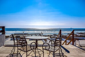 Eine Terrasse mit Blick auf den Ozean, ausgestattet mit runden Tischen und Metallstühlen.