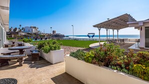 Een terras met buitenmeubilair, uitzicht op het strand en een pergola.