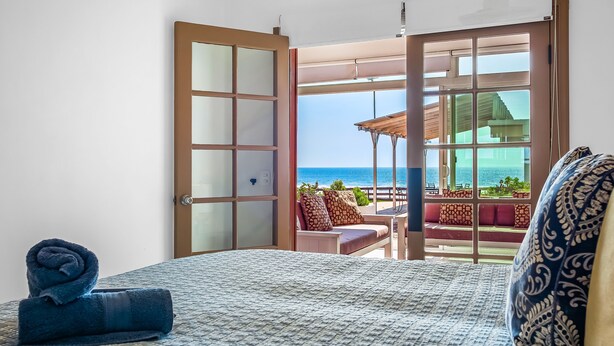 Een hotelkamer met een bed, uitzicht op zee en een balkon met zitplaatsen buiten.