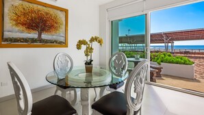 A dining area with a glass table, white chairs, a potted plant, and a painting of a tree. - Bright dog-friendly villa with beach views, private patio, outdoor pool, kitchen (Rosarito)
