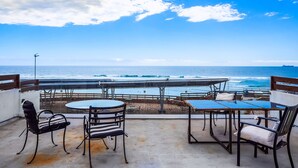 A terrace with a view of the ocean, featuring round tables and chairs, a railing, and a sandy beach area. - Bright dog-friendly villa with beach views, private patio, outdoor pool, kitchen (Rosarito)