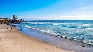 A beach with a clear sky, waves, and a few people walking. - 2-story dog-friendly villa with outdoor pool, patio, 2 balconies, streaming, AC (Rosarito)