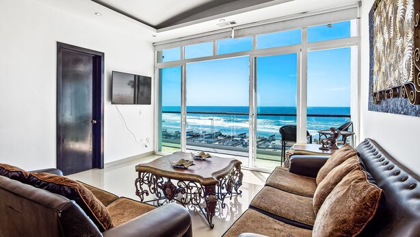 A spacious living room with a large window overlooking the ocean, a dark door, and a flat-screen TV mounted on the wall. - 2-story dog-friendly villa with outdoor pool, patio, 2 balconies, streaming, AC (Rosarito)