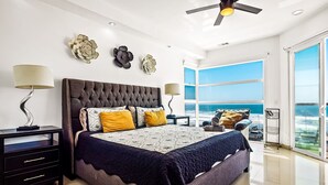 A bedroom with a large bed, two bedside tables, a ceiling fan, and a view of the ocean through large windows. - 2-story dog-friendly villa with outdoor pool, patio, 2 balconies, streaming, AC (Rosarito)