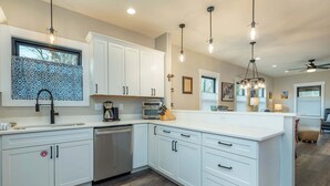 Una cocina moderna con armarios blancos, lavavajillas integrado e iluminación colgante.