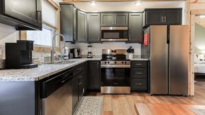 A modern kitchen with stainless steel appliances, dark cabinetry, and a wooden ceiling.