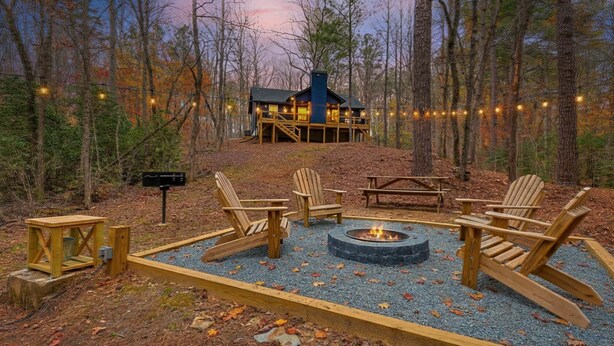 A cabin with a fire pit and Adirondack chairs in a forest setting.