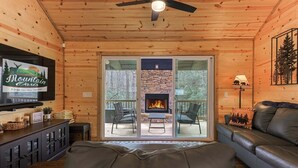 A cabin interior with a stone fireplace, a television, a leather sofa, and a deck with outdoor seating.