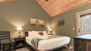 A bedroom with a bed, two bedside tables with lamps, a chair, a rug, and a door with a view of trees.