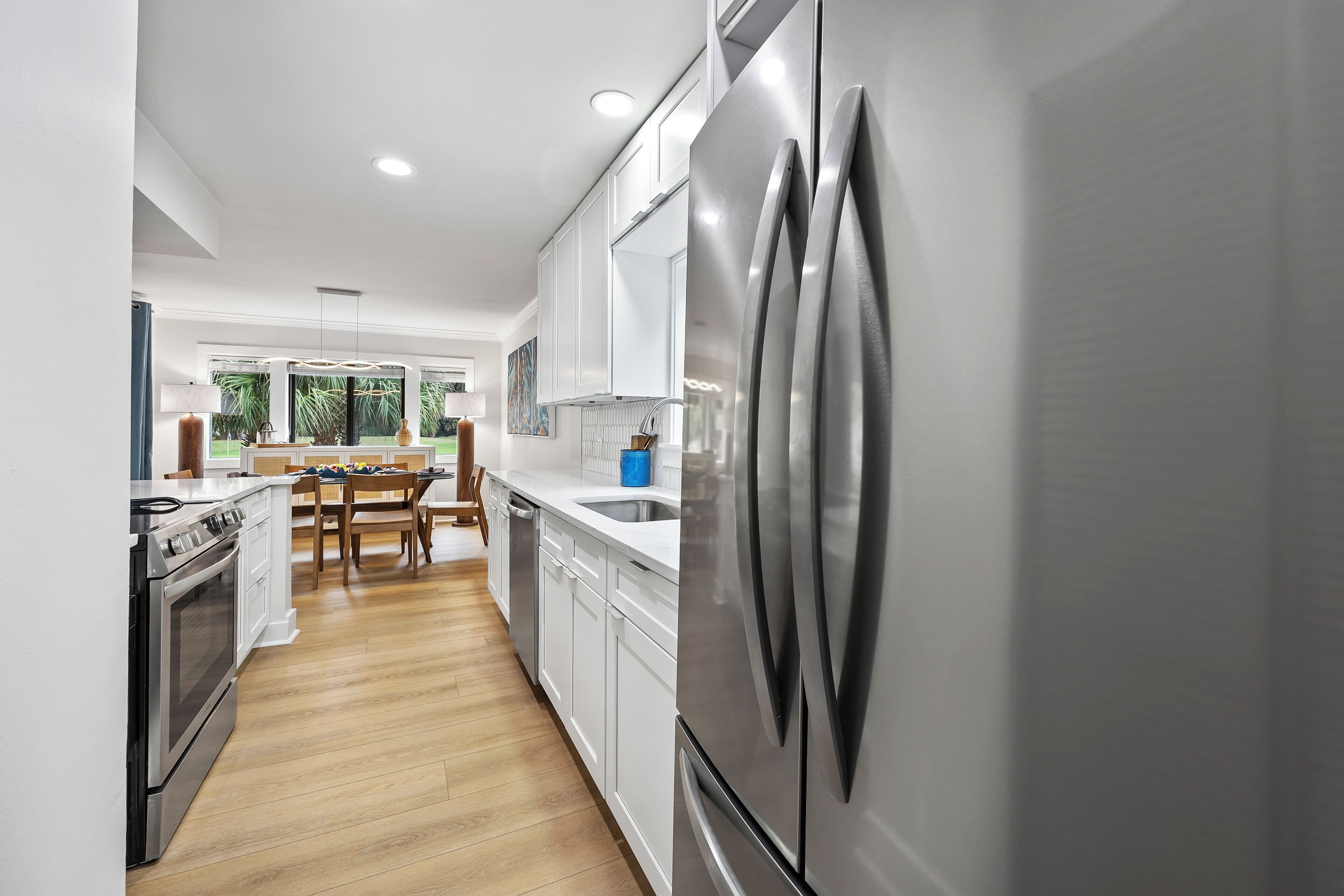A modern kitchen with stainless steel appliances, white cabinetry, and a wooden dining table.