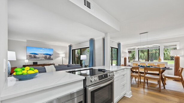 Een moderne keuken met een ingebouwde oven, een eethoek met een houten tafel en stoelen, en een groot raam met uitzicht op groen.