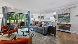 Een moderne woonkamer met een bank, fauteuils, een glazen salontafel en uitzicht op de omgeving.