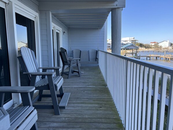 Une terrasse en bois, dotée de chaises et d’une rambarde, qui offre une vue sur une étendue d’eau.