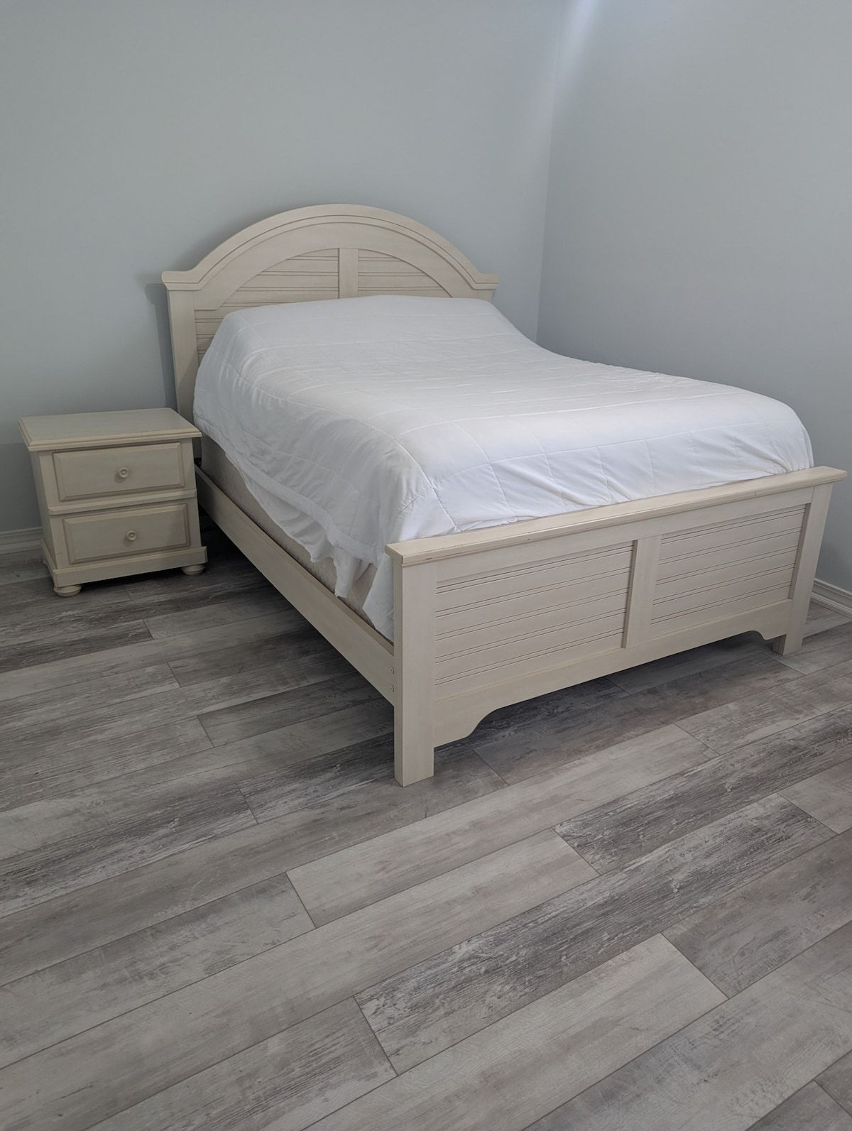 A single bed with a headboard and footboard, a bedside table with drawers, and a grey herringbone-patterned floor.