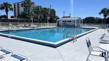A swimming pool with a tiled deck, lounge chairs, and a small building in the background.