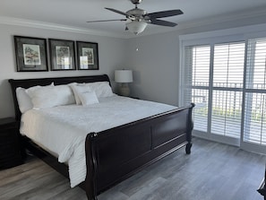 A bedroom with a dark wooden bed, white bedding, a ceiling fan, and a view through large windows. - A 11 Sundown Condominiums (Pensacola)