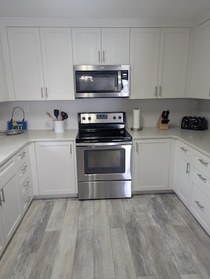 A kitchen with white cabinets, a microwave, a stove, and a toaster. - A 11 Sundown Condominiums (Pensacola)