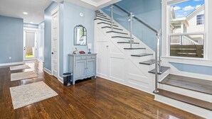 Un pasillo amplio con pisos de madera, una escalera con barandillas de vidrio y vistas al exterior.