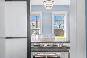 A dining area with a table and chairs, a bench, and a view through large windows. - Tipsy Turtle | Beachy Galveston Getaway (Galveston)