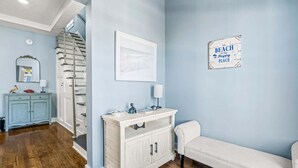 Un pasillo con pared azul claro, un banco blanco, un armario blanco con lavabo, un espejo y un mapa enmarcado.