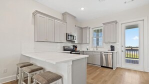 A kitchen with white cabinets, a central island with stools, a microwave, and a dishwasher.