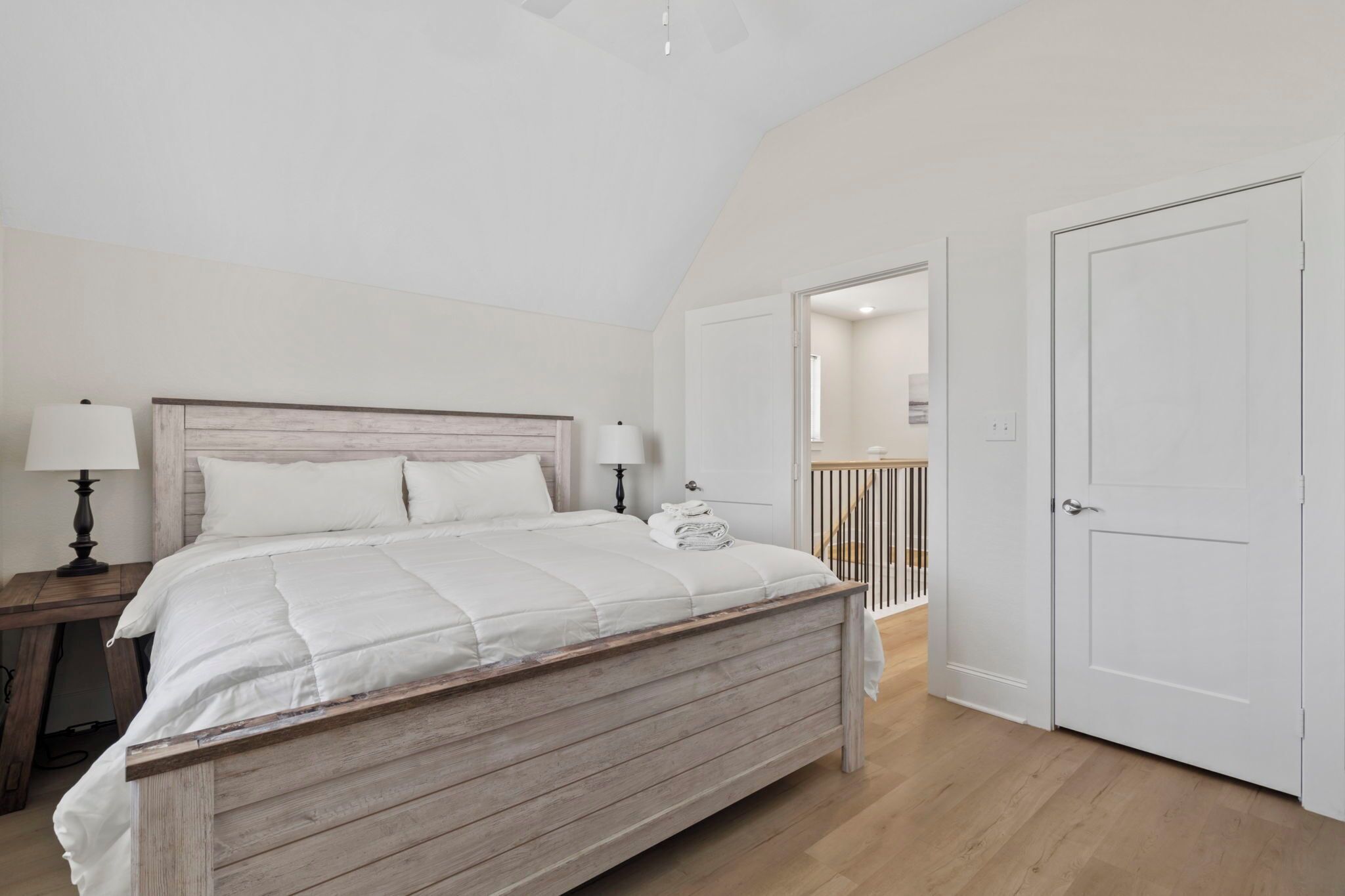 Une chambre à coucher avec un lit en bois, une table de chevet, une lampe et une porte donnant sur une autre pièce.
