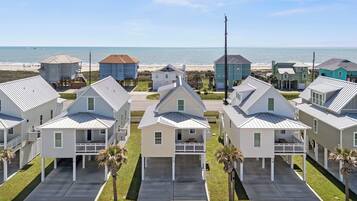 Un quartier résidentiel situé sur la côte, avec des maisons dotées de toits à pignon, une plage en arrière-plan et un ciel dégagé.