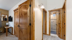 Un couloir avec des portes en bois, une petite table avec une lampe et un espace douche aux murs carrelés.