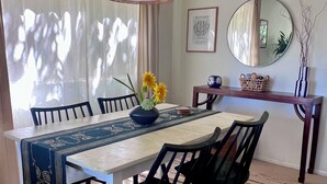 Een eetgedeelte met een tafel, stoelen, een hanglamp, een spiegel en een lijst met een kunstwerk aan de muur.
